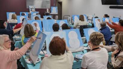 a large group of pepole paint on canvases together in a winery room